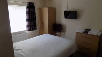 A bedroom with a bed, a wardrobe, a television, and a window with curtains.
