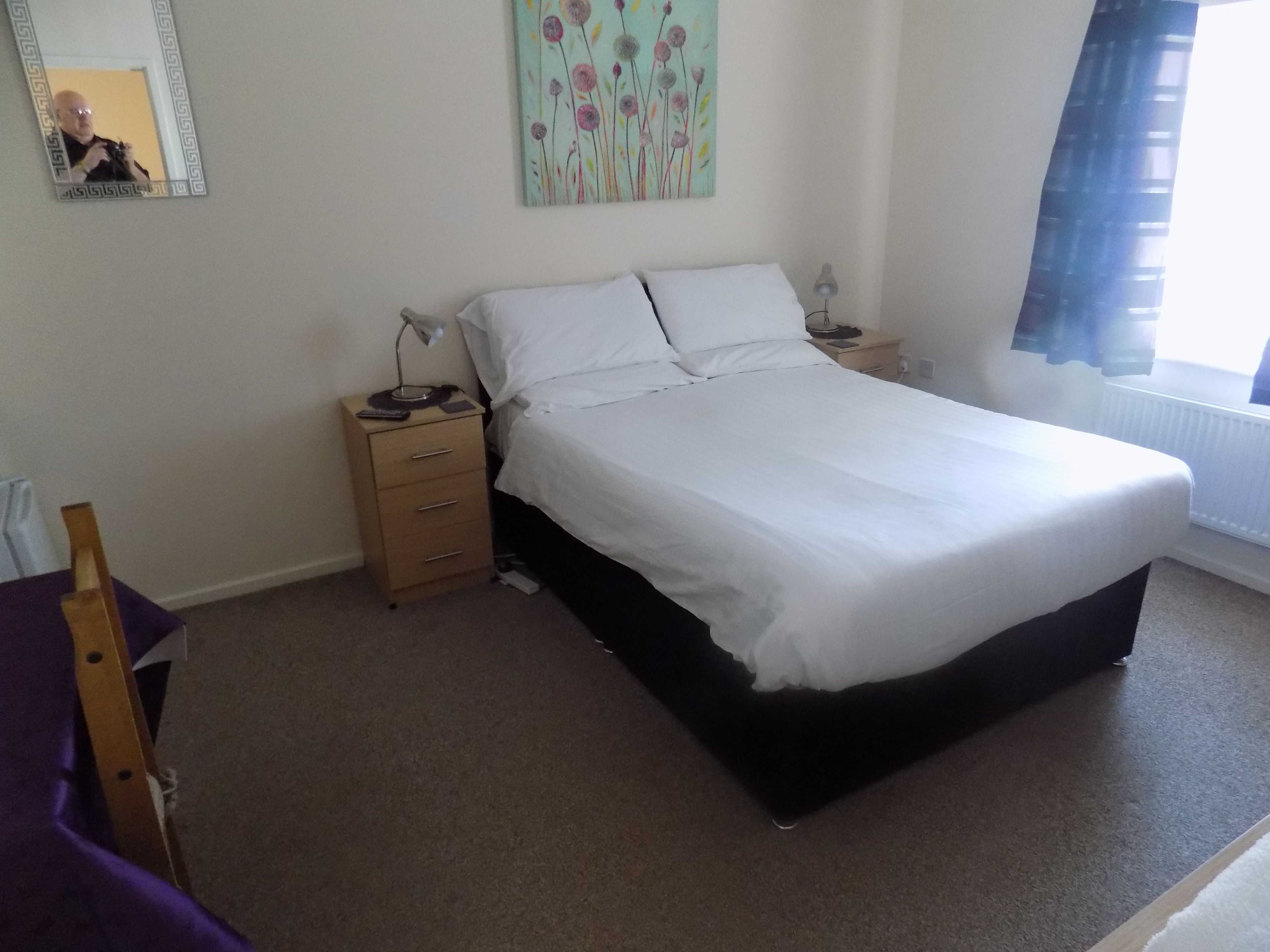 A bedroom with a bed, a nightstand, a dresser, a mirror, and a window with curtains.