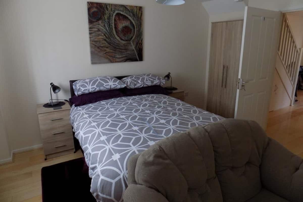A bedroom with a bed, a nightstand, a lamp, a chair, and a door leading to another room.