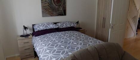 A bedroom with a bed, a nightstand, a lamp, a chair, and a door leading to another room.