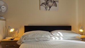 A hotel room with a bed, two bedside lamps, a wall-mounted fan, and a painting. - A Home From Home 2 (Plymouth)