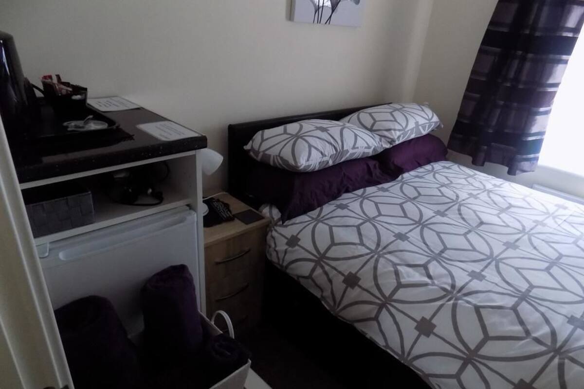 A bedroom with a bed, a nightstand, a dresser, and a desk with a computer and a lamp.