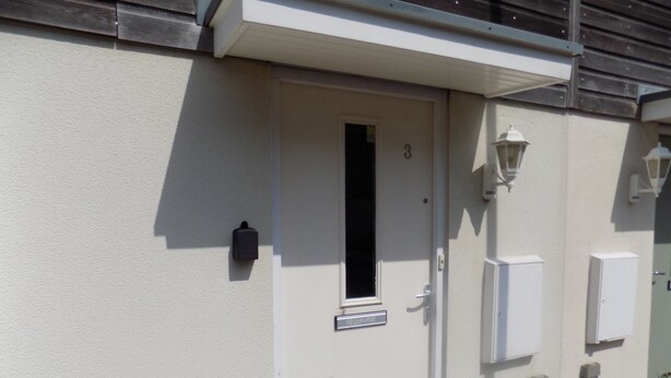 A white door with a small window and a number '3' above it. There are two wall-mounted light fixtures and a small mailbox on the wall. - A Home From Home 2 (Plymouth)