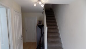 A staircase with carpeted steps leading to a door marked with the number 1. A vacuum cleaner is positioned against the wall near the staircase. - A Home From Home 2 (Plymouth)