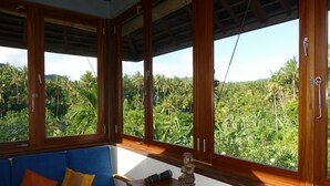 Une pièce avec un canapé bleu, un meuble en bois et de grandes fenêtres donnant sur un paysage verdoyant.