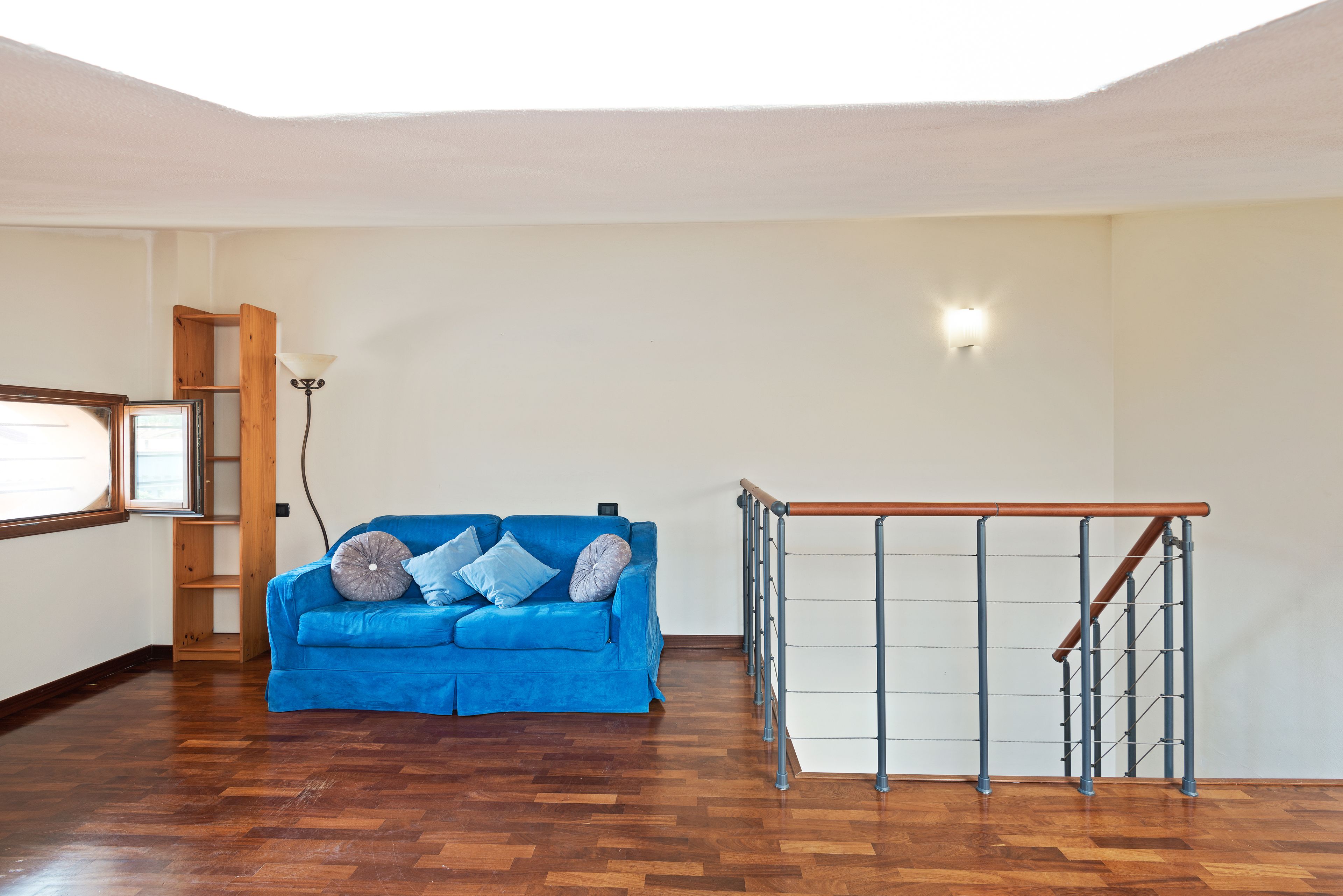 A room with a blue sofa, wooden flooring, a wooden ladder, and a metal railing.