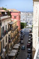 Una stretta via fiancheggiata da auto parcheggiate e palazzi con balconi, che conduce a una marina piena di barche.