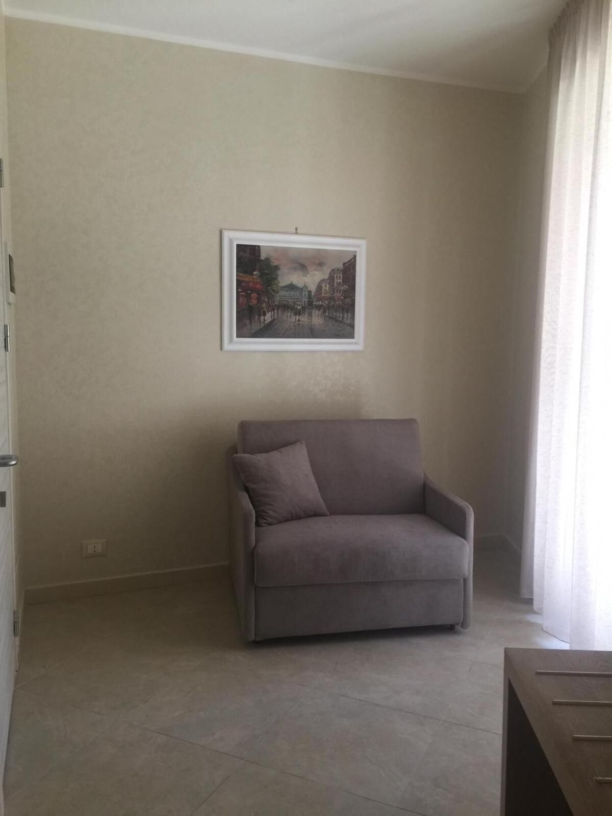 En stue med en beige sofa, et billede i ramme på væggen og et vindue med gardiner.