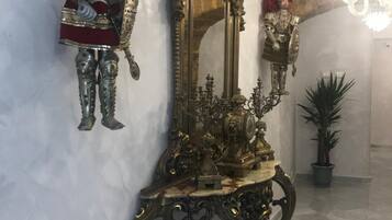 A marble-floored hallway with ornate gold-framed mirrors and a decorative metal figure.