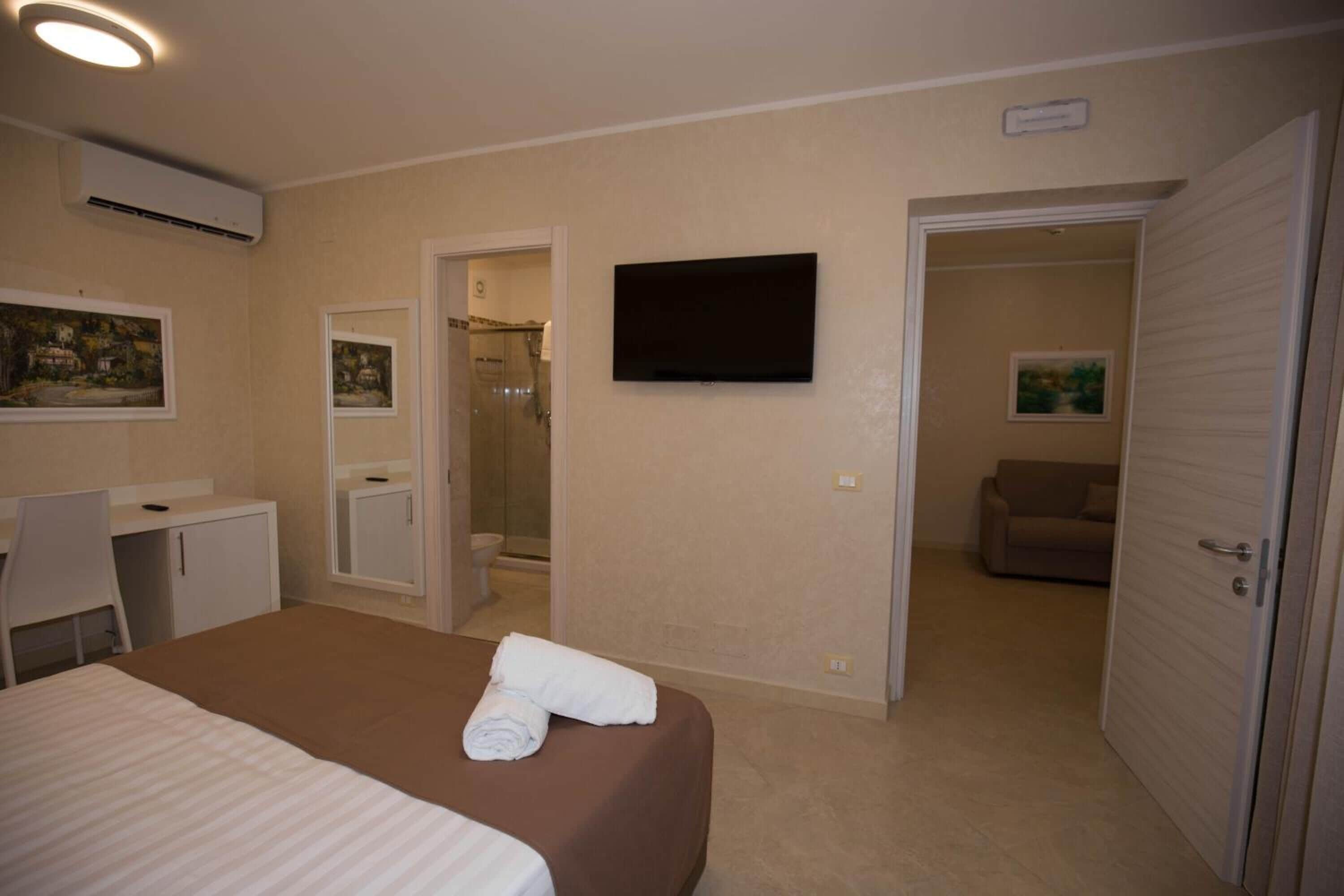 Hotellihuone, jossa on sänky, työpöytä, televisio ja suihkutila.