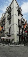 Un edificio d'angolo con diversi balconi, piante in vaso e una bandiera.