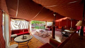 A tented room with a red carpet, a round table with a teapot, and a sofa. - Relais Esmeralda (Lalla Takarkoust)