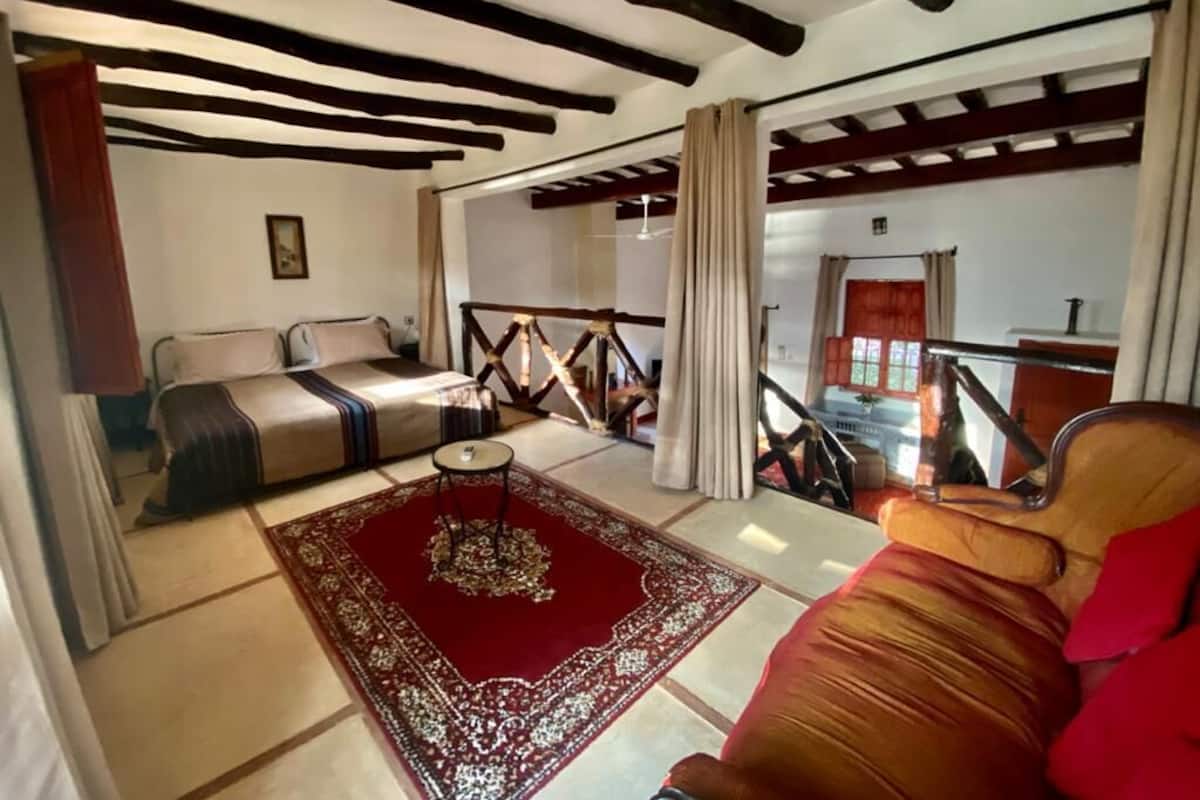 A room with a bed, a sofa, a red rug, and a staircase leading to an upper level.