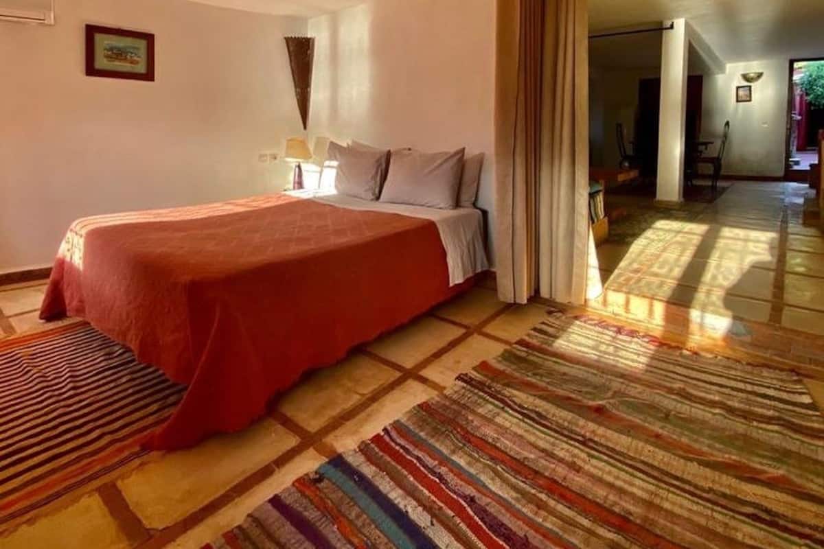 A hotel room with a large bed, a colorful striped rug, and a view of the hallway.