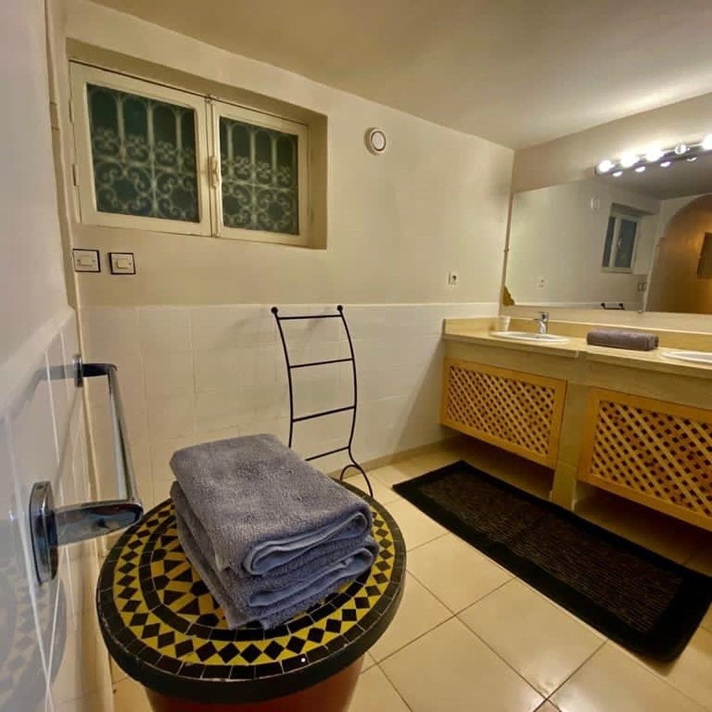 A bathroom with a tiled floor, a sink with a mirror, a towel rack, and a window with decorative glass.