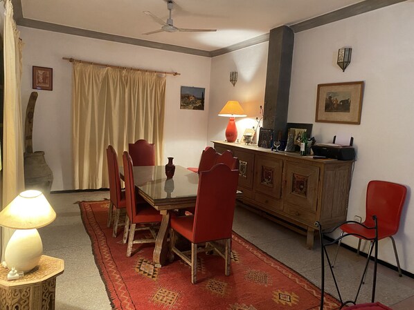 A dining area with a glass-top table, red chairs, a wooden cabinet, and a red rug.