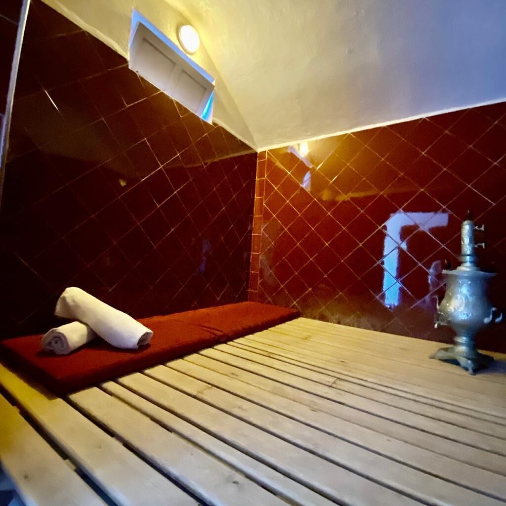 A sauna room with a wooden bench, a red towel, and a metal heater.