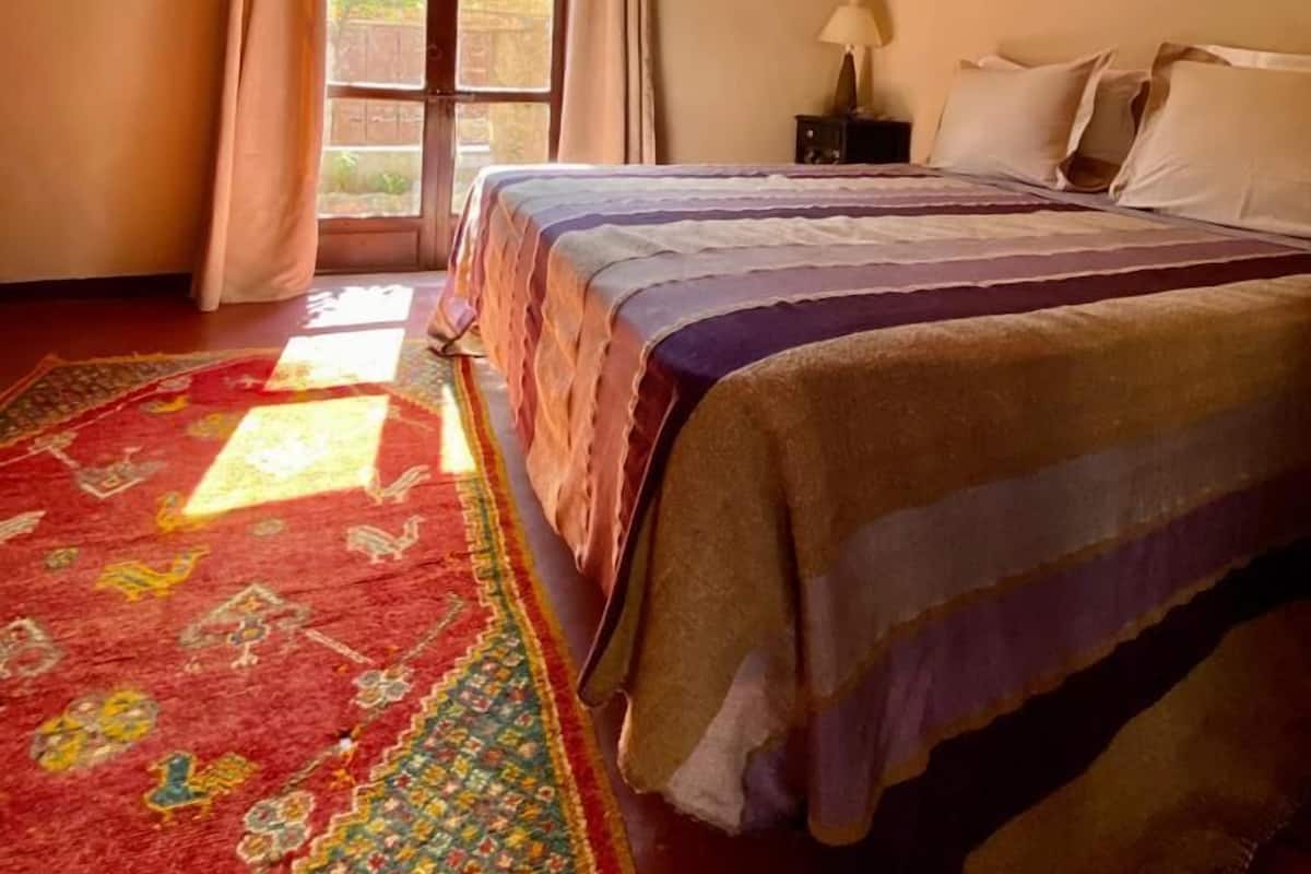 A bedroom with a bed, a window with curtains, a ceiling fan, and a painting on the wall.