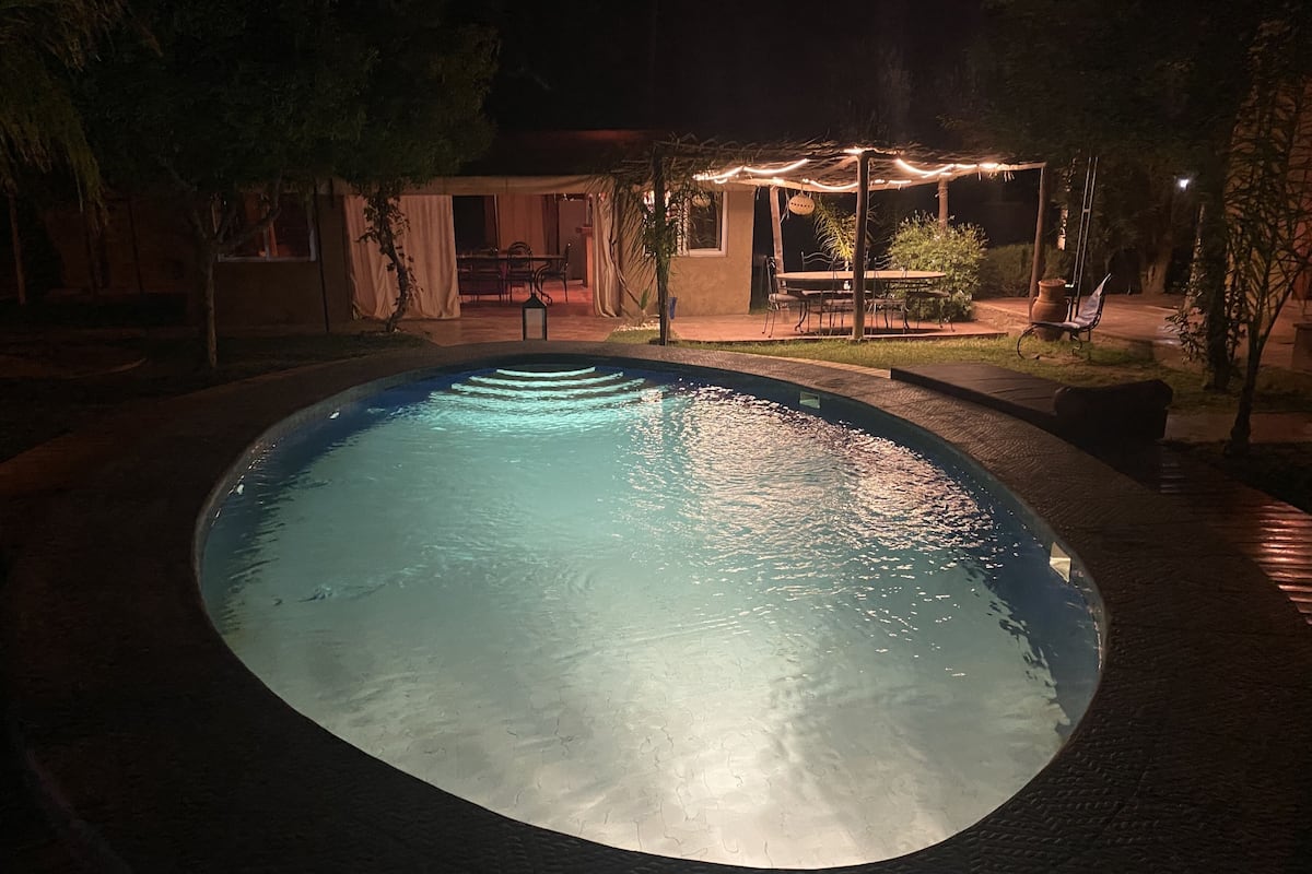 A swimming pool at night with a pergola and outdoor seating area.