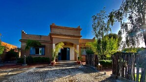 A building with a stone entrance, a wooden fence, and a clear blue sky. - Relais Esmeralda (Lalla Takarkoust)