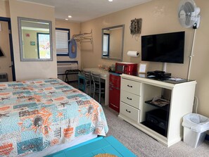 Ein Schlafzimmer mit Bett, Schreibtisch, Fernseher, Ventilator und Mülleimer.