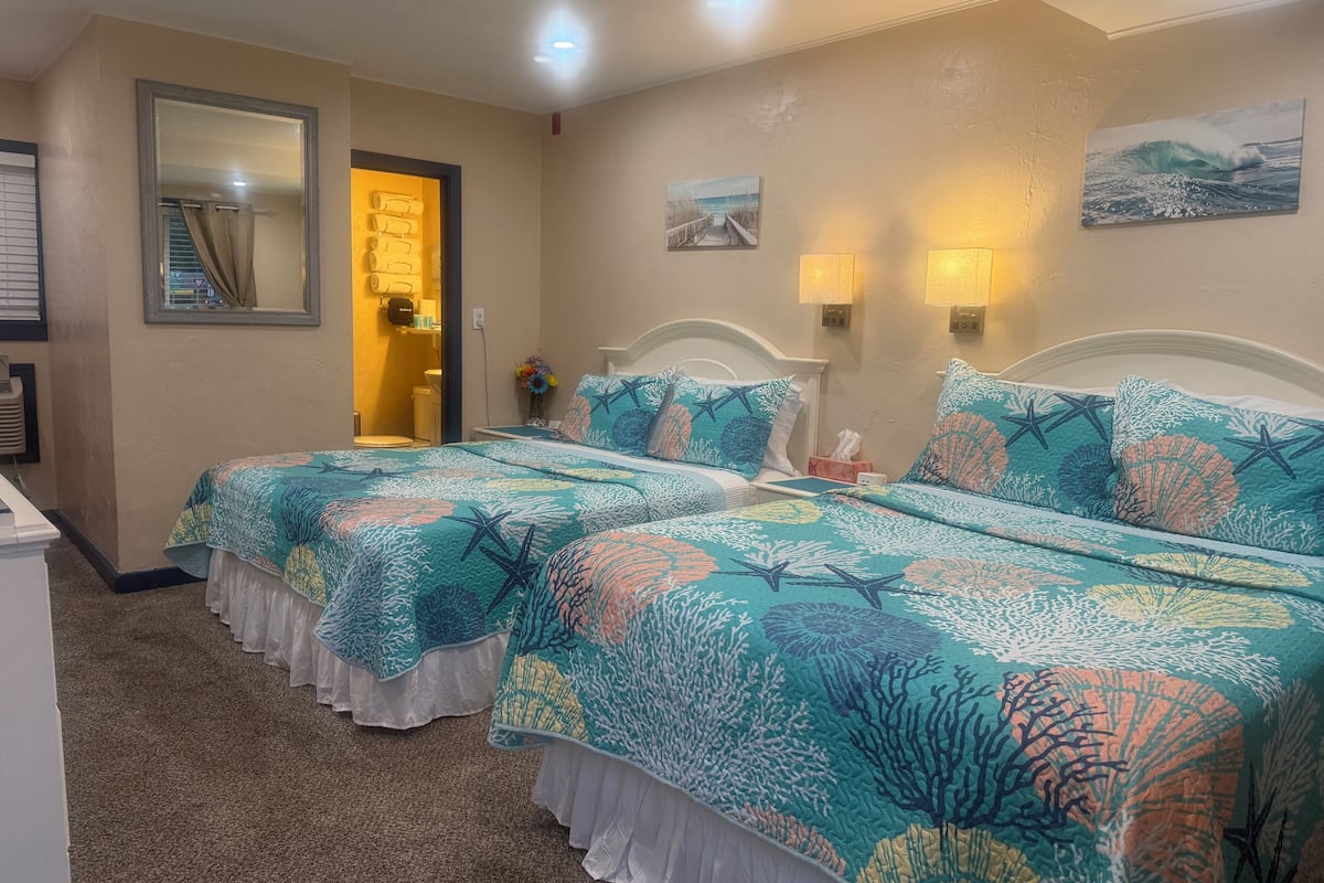 Quarto de hotel com duas camas, um banheiro, um espelho e um quadro na parede.