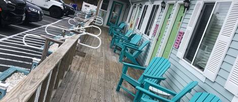A wooden deck with teal Adirondack chairs, a water tower in the background, and a row of buildings with green doors.
