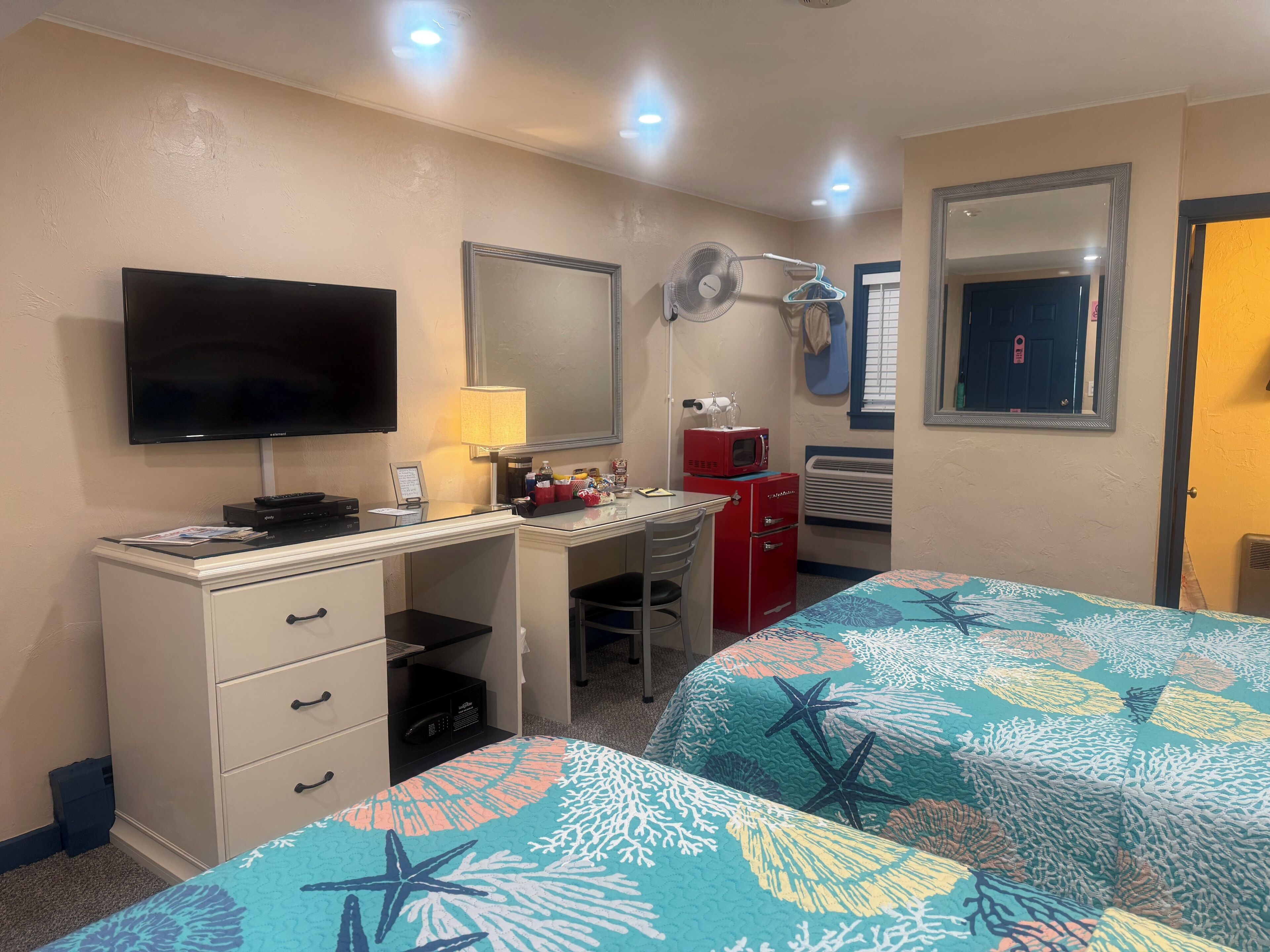A hotel room with a desk, television, and two beds with starfish-themed bedding.