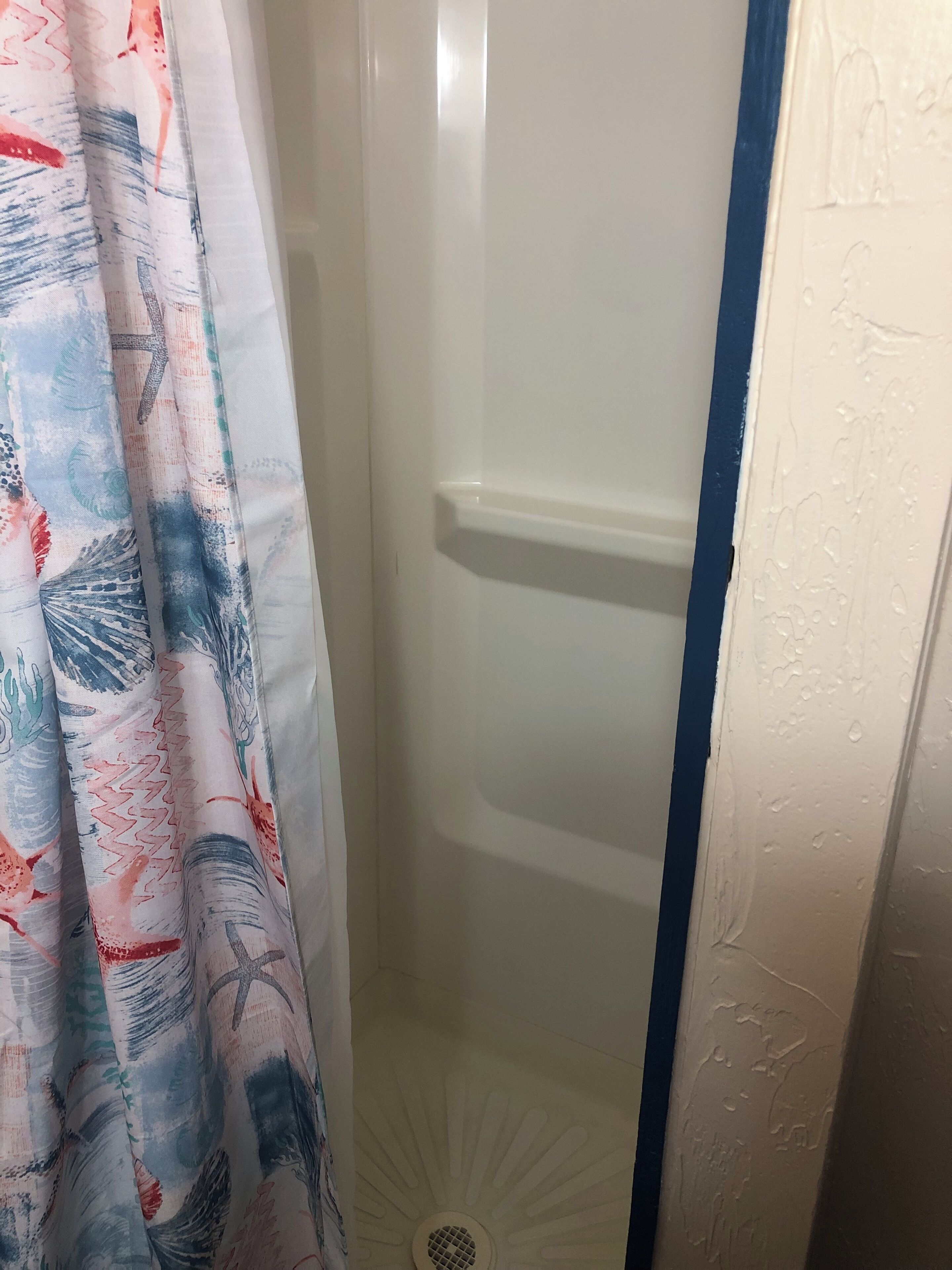 A shower area with a white door, a blue vertical stripe on the wall, and a shower curtain with a colorful abstract pattern.