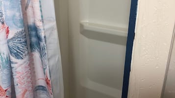 A shower area with a white door, a blue vertical stripe on the wall, and a shower curtain with a colorful abstract pattern.