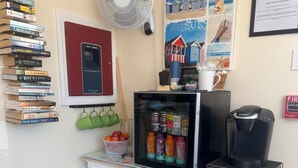 A kitchenette with a coffee maker, a fan, a refrigerator, and a bookshelf with books. - The Inn at Buzzards Bay (Buzzards Bay)
