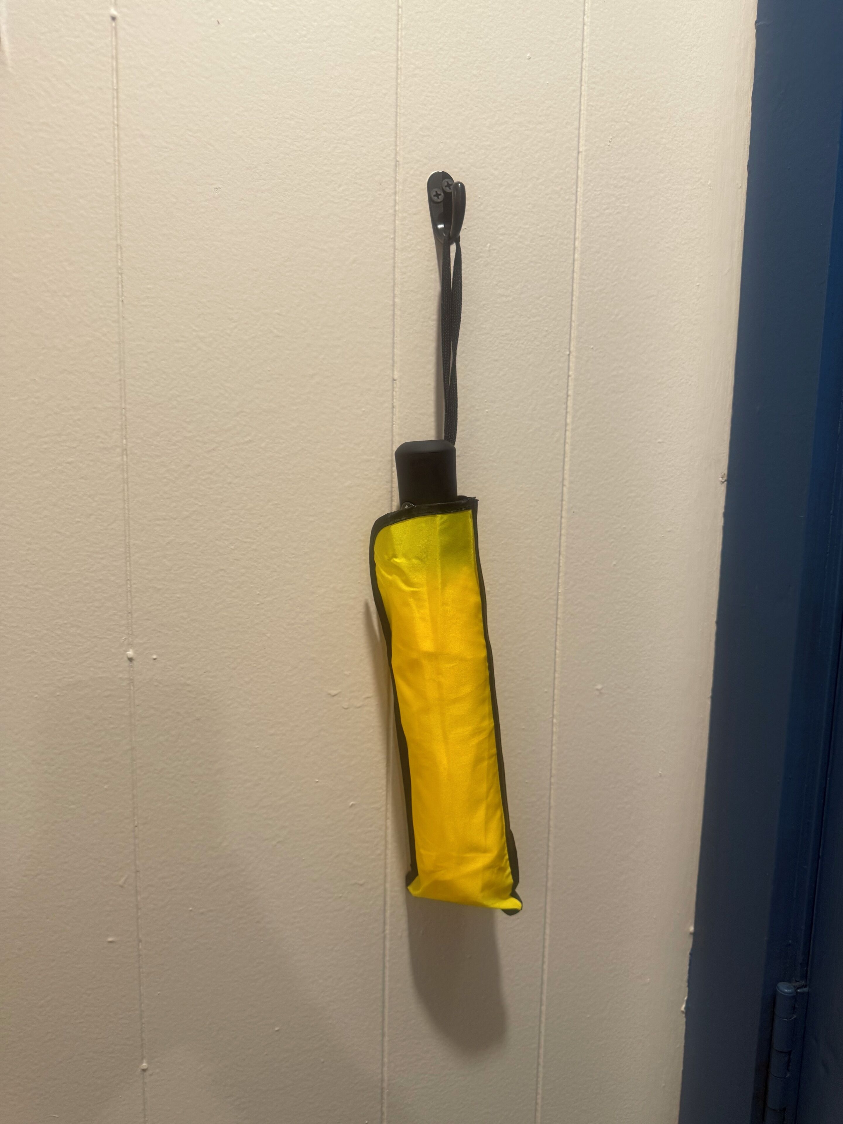 A yellow umbrella hanging on a white door.
