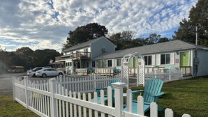 A row of mobile homes with a white picket fence, green doors, and outdoor seating. - The Inn at Buzzards Bay (Buzzards Bay)