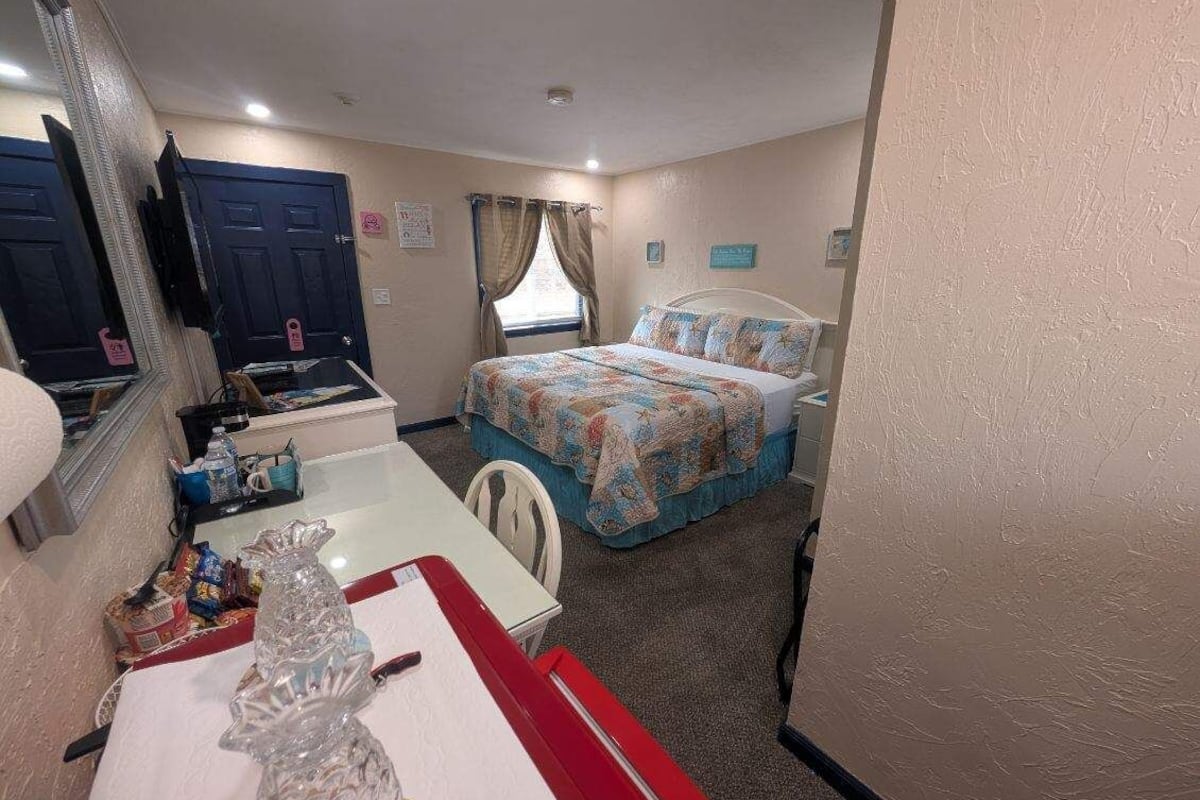 Quarto com cama, escrivaninha, cadeira, espelho e janela com cortinas.