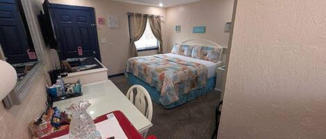 A bedroom with a bed, a desk, a chair, a mirror, and a window with curtains.