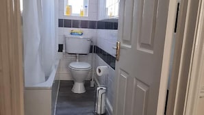A narrow hallway leading to a bathroom with a toilet, sink, and bathtub. - Comfort Rooms (Plymouth)