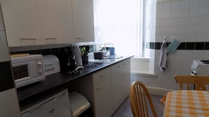 A compact kitchen with white cabinets, a microwave, a bread maker, and a sink. - Comfort Rooms (Plymouth)