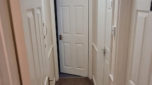 A hallway with white doors, carpeted floor, and a ceiling light fixture. - Comfort Rooms (Plymouth)