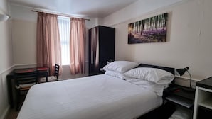 A hotel room with a bed, a desk, a chair, a wardrobe, a painting, and a kettle. - Comfort Rooms (Plymouth)