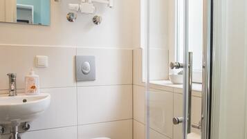 Un baño moderno con cabina de ducha de vidrio, un lavamanos blanco y un inodoro.