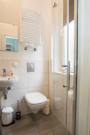 A modern bathroom with a glass shower enclosure, a white sink, and a toilet. - Micro Appartments Katz (Nuremberg)