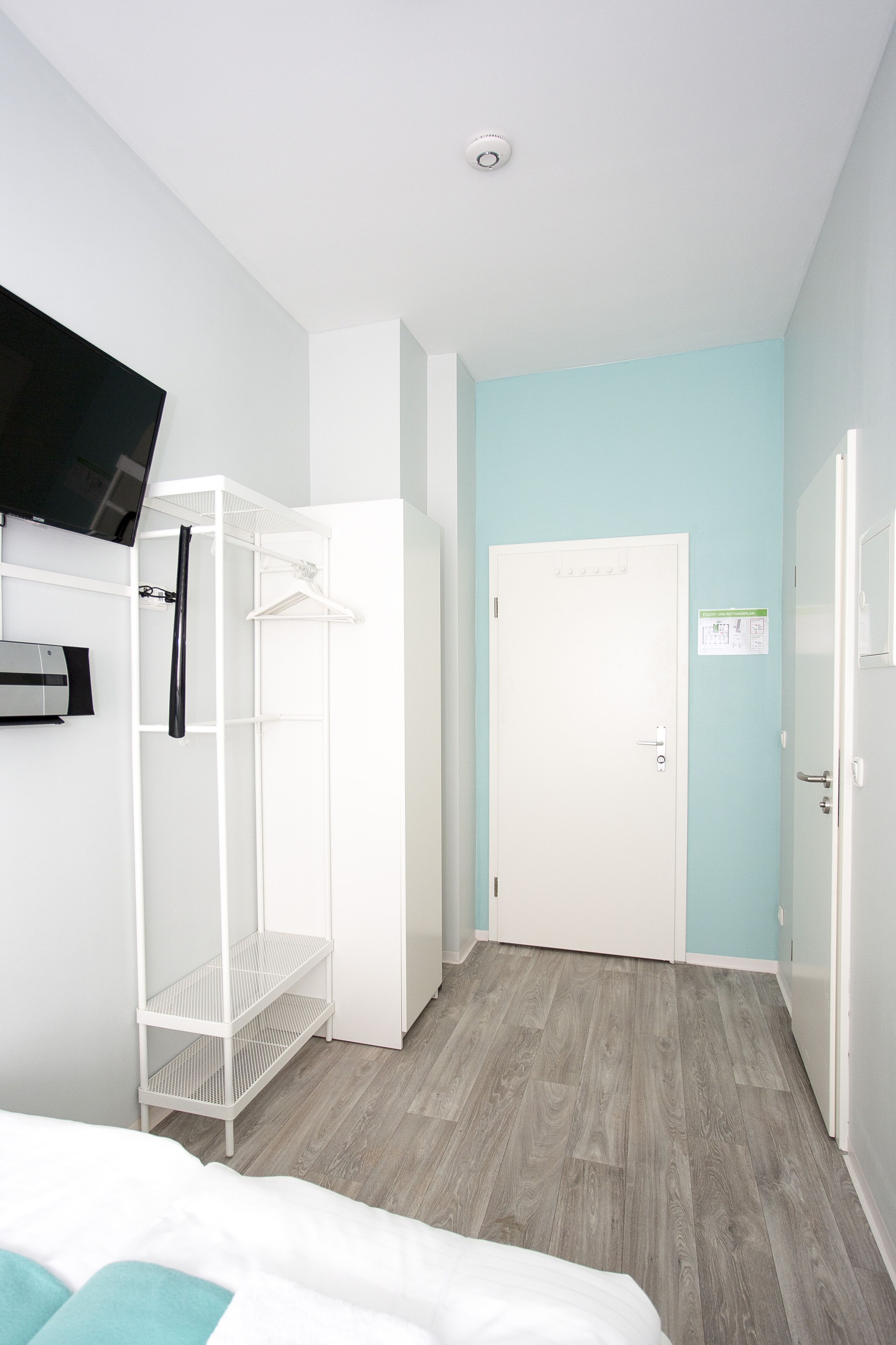 Un dormitorio con cama, un armario blanco, una estantería blanca y un televisor montado en la pared.