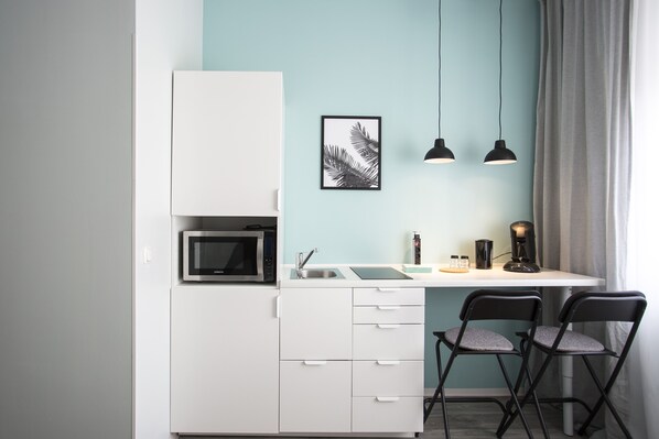 A compact kitchenette with a microwave, sink, and two chairs. - Micro Appartments Katz (Nuremberg)