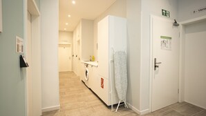 Un couloir d’hôtel avec un lave-linge, une planche à repasser et une porte portant un panneau indiquant la sortie de secours.