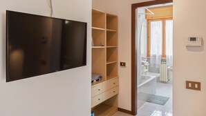 Een moderne badkamer met een badkuip, toilet en wastafel. Er is een houten wandplank met een aan de muur bevestigde televisie.