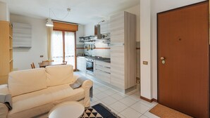 Een moderne keuken met witte kastjes, een eetgedeelte met een tafel en stoelen, en een woonkamer met een bank en een salontafel.