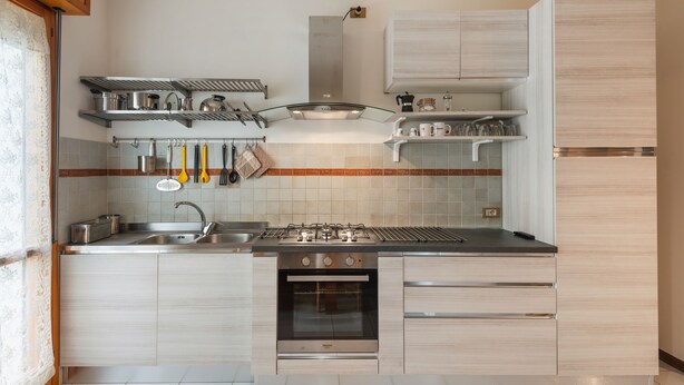 Een moderne keuken met roestvrijstalen apparatuur, houten kastjes en een betegelde achterwand.
