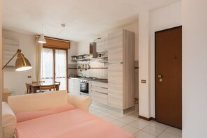 Eine moderne Küche mit weißen Schränken, eine Essecke mit Tisch und Stühlen sowie ein Schlafzimmer mit Bett und Lampe.