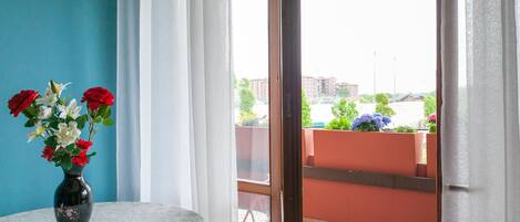Una habitación con vistas a un balcón, una mesa con un jarrón de flores y una ventana con cortinas.