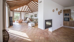 A spacious living area with a fireplace, wooden ceiling beams, and a kitchen with modern appliances. - Casa Serena | 6 Bedrooms | Country House |  Estoi (Estoi)